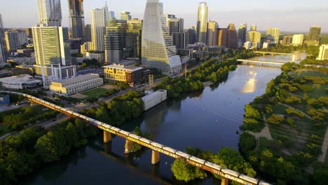 Aerial-view-of-a-long-train-arriving-in-Austin-Texas,-sunny-summer-evening-in-USA---tilt,-drone-shot