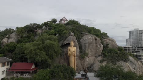 Retroceso-De-La-Estatua-Dorada-De-Buda-De-Pie-Sobre-Una-Roca,-Cerca-De-La-Playa-De-Takiap,-Tailandia