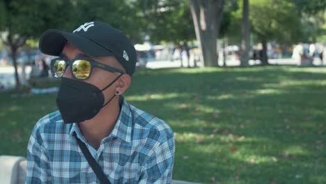 Young-stylish-Nepali-man-sitting-in-park-on-summer-day-wearing-mask