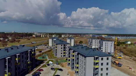 Aerial-drone-backward-moving-shot-over-a-residential-complex-under-construction-with-the-view-of-a-parking-lot-in-the-center-on-a-cloud-day-in-timelapse