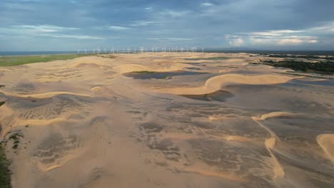 Beautiful-drone-take-of-dunes-in-northeast-brazil-at-dusk,-magic-light-and-wind-turbines-in-the-background