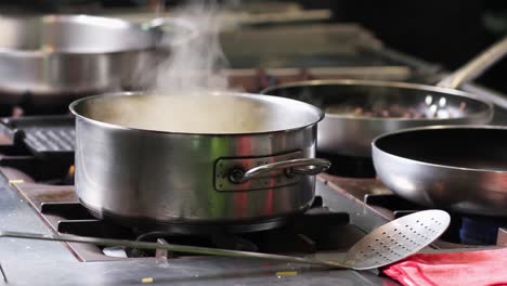 Water-steam-coming-from-a-boiling-casserole,-surrounded-by-cooking-pans-in-professional-and-commercial-kitchen-at-a-high-cuisine-restaurant