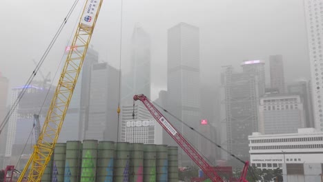Skyscraper-corporate-buildings-in-Hong-Kong-during-rainstorm,-construction-site-tower-cranes-in-foreground