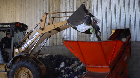 A-bulldozer's-bucket-dumping-the-waste-into-a-conveyor-belt's-hopper-inside-a-waste-processing-plant
