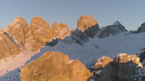 Glowing-rugged-snowy-Tre-Cime-mountain-peaks-aerial-view-reveal-golden-sunrise-over-distant-ridge
