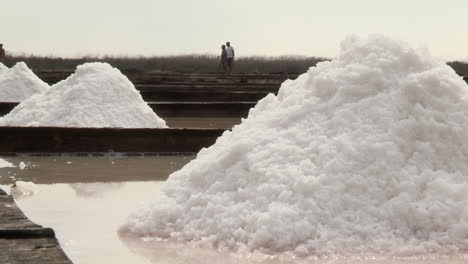 Beautiful-heaps-of-salt-extracted-from-the-salt-pan,-in-the-background-three-men-working-in-the-salt