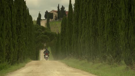 Man-riding-a-motorbike-to-a-beautiful-country-estate-in-Tuscany-in-bright-sunshine