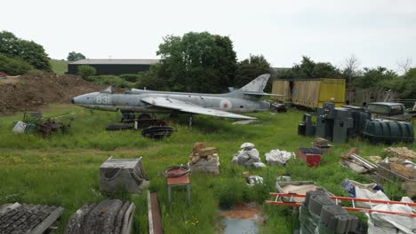 Junk-yard-British-field-with-discarded-Hawker-hunter-fighter-jet-side-low-aerial-view
