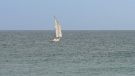 Ein-Segelboot-Mit-Weißem-Segel-Auf-See,-Das-Sich-Nach-Rechts-Vom-Meer-Entfernt