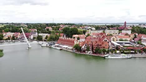 Touristic-city-in-Warmian-Masurian-with-beautiful-calm-lake-in-summer-with-yachts-and-tourists,-bridges-and-old-historic-buildings