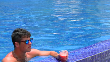 Ein-Junger-Erwachsener-Mann-Im-Pool-Des-Resorts-Nippt-An-Einem-Erdbeer-Daquiri-Getränk-Und-Blickt-Auf-Das-Wunderschöne-Meer