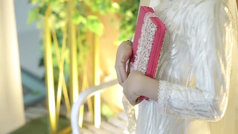 Young-Pious-Beautiful-Muslimah-Woman-Wearing-white-veil---Holding-and-Hugging-The-Holy-Book-Of-Quran-As-Islamic-Religion-Basic-Universal-Knowledge-Source