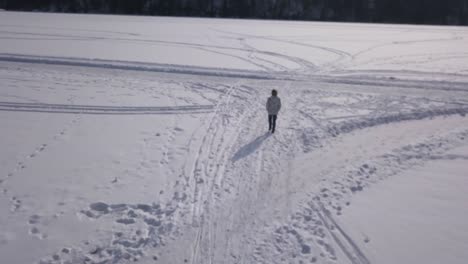 Zoom-in-tracking-aerial-shot-of-blonde-girl-strolling-on-frozen-lake