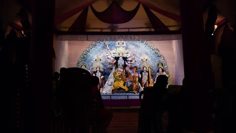 Escultura-De-Dioses-Y-Diosas-Indias-Durga-En-Pandal-Y-Silueta-De-Personas-Disfrutando-Del-Festival-Durga-Puja-Por-La-Noche