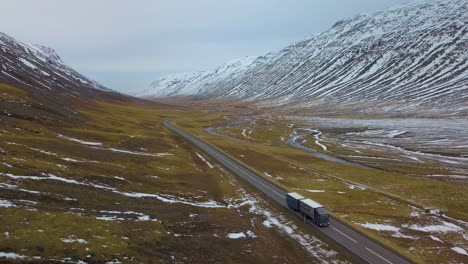 Aerial-view-of-transport-truck-driving-down-highway-in-between-snowy-mountains