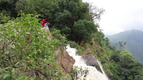 Man-sitting-on-a-cliff-watching-a-waterfall