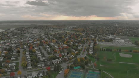 Aerial-footage-rising-from-a-view-of-a-tennis-court-to-the-view-of-a-huge-sunset-over-a-small-town-with-sun-beams-showing-through-the-clouds-and-lots-of-vehicles-on-turning-roads