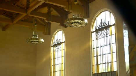 Tilting-down-from-the-ornate-ceiling-chandeliers-and-golden-windows-in-the-empty-halls-of-Union-Station-in-Los-Angeles,-California