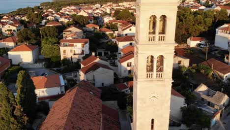 A-drone-shot-of-a-church-and-a-belltower-in-Supetar,-the-island-of-Brac,-Croatia