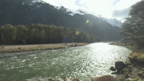 Running-river-surrounded-by-snow-capped-mountains-and-lush-green-forrest-on-a-sunny-winters-day-in-New-Zealand