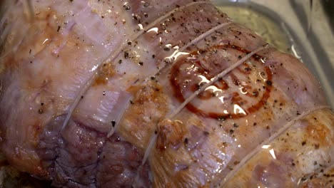 Slow-motion-close-up-of-pouring-oil-on-top-of-a-halfway-cooked-a-joint-of-pork-in-a-glass-oven-dish