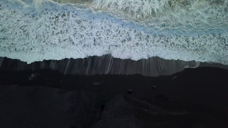 Top-down-drone-aerial-of-waves-coming-up-onto-the-black-sand-beach-near-Vik-in-Iceland