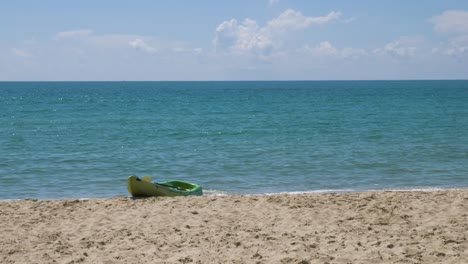 Slow-motion-video-of-an-empty-green-kayak-docked-on-the-shore-of-a-beach-with-a-beautiful-sunny-and-glimmering-ocean-view-horizon