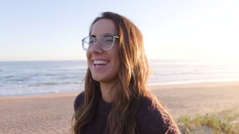 Young-girl-with-glasses-smiling-and-laughing-at-beach-during-sunset