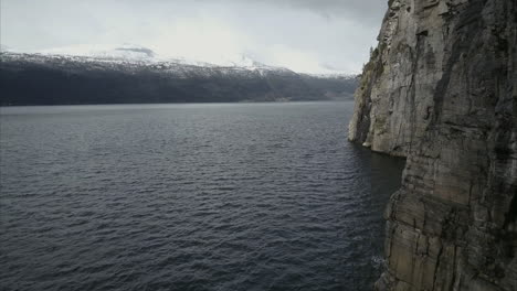 Flug-über-Den-Norwegischen-Fjord-Nahe-Der-Felsigen-Küste,-Berge-Mit-Schnee-Im-Hintergrund,-Luftaufnahme