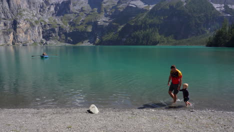 Father-and-son-hold-hands-while-playing-at-a-clear-blue-mountain-lake-in-the-swiss-alps