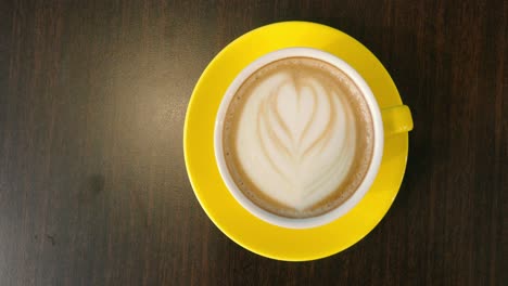 Overhead-view-of-coffee-latte-in-a-yellow-mug-and-saucer-on-a-table