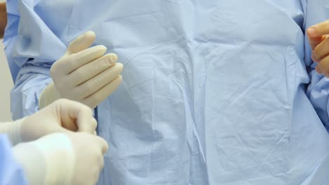 Nahaufnahme-Der-Hände-Eines-Chirurgen,-Während-Ein-Anderer-Arzt-Beim-Anziehen-Steriler-Handschuhe-Für-Die-Operation-Hilft