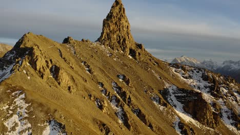 Aerial-orbit-climbing-around-rocky-summit,-Alpine-landscape-in-the-background