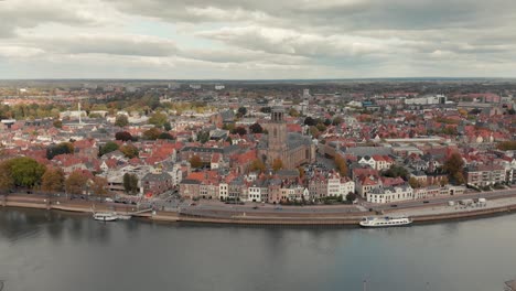 Aerial-drone-shot-closing-in-on-the-Dutch-medieval-city-of-Deventer-from-the-other-side-of-the-river-IJssel-on-a-cloudy-day