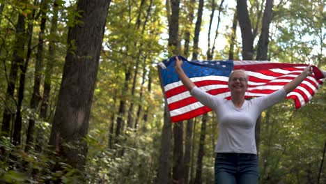 Pretty-blonde-woman-running-through-a-forest-with-a-flag-flying-behind-her-with-the-sun-sparking-through-the-trees