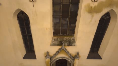 A-pedestal-approaching-drone-shot-capturing-the-entrance-and-a-large-window-above-it,-of-a-vintage-architectural-church-in-the-city-of-Sighisoara-on-an-afternoon
