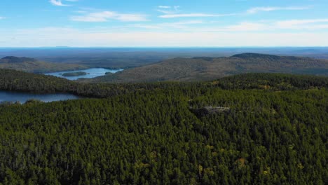 Aerial-drone-shot-sliding-right-over-a-large-green-forest-with-lakes-and-a-rocky-outcrop-in-the-Maine-wilderness
