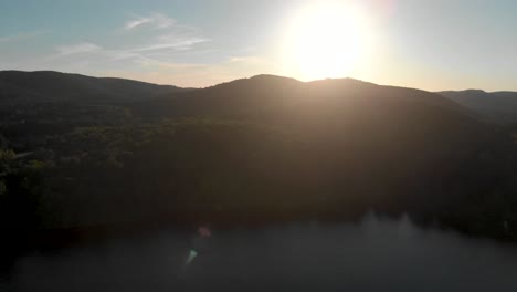 Slow-aerial-flight-over-a-canadian-lake-in-quebec-which-is-surrounded-by-trees-at-sunrise-with-the-sun-shining-over-the-hill-and-trees