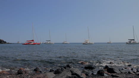 Catamaranes-Estacionados-En-El-Mar,-Cerca-De-Una-Playa-Rocosa