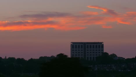 Wide-dawn-sunrise-timelapse-of-a-tall-office-building-and-trees-silhouetted-into-the-foreground