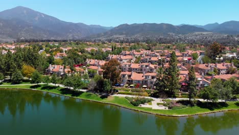 Drone-Aéreo-Elevándose-Sobre-El-Lago-Comunitario-Y-Condominios-Con-Montañas-Como-Fondo