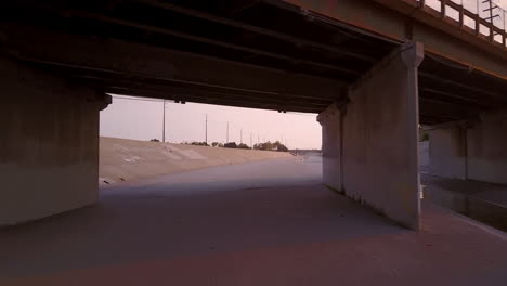 Low-Angle-fly-under-bridge-in-Los-Angeles-river-at-dusk