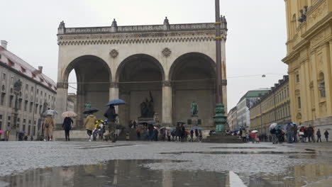 Wide-Angle:-Multiple-groups-of-tourists-walking-around-the-odeonsplatz-during-the-rain