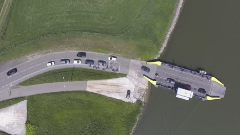 A-topdown-drone-shot-of-a-ferry,-loading-off-cars-en-people-from-a-river-to-land,-panning-down,-in-the-Netherlands