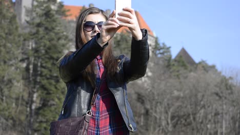 Lovely-young-woman-with-brown-hair-making-selfie-pictures-in-a-public-park-on-a-nice-sunny-afternoon