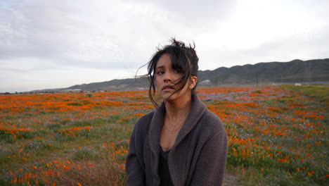 Young-beautiful-woman-crying-and-looking-sad-in-a-meadow-of-wild-flowers-under-dark-cloudy-skies-in-slow-motion