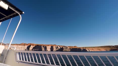 From-the-deck-of-a-houseboat,-the-blue-waters-and-sandstone-buttes-pass-by,-Lake-Powell,-Page,-Arizona