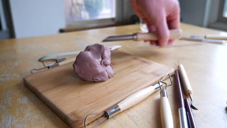 An-artist-preparing-his-sculpting-tools-and-cutting-a-piece-of-brown-modeling-clay-as-he-begins-his-project-in-the-art-studio
