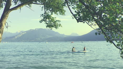 People-boating-on-Lake-Annecy,-third-largest-lake-in-France,-peaceful-and-sunny-day,-with-a-mountain-landscape-background
