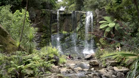 People-sitting-under-Mokora-Falls,-Auckland,-New-Zealand